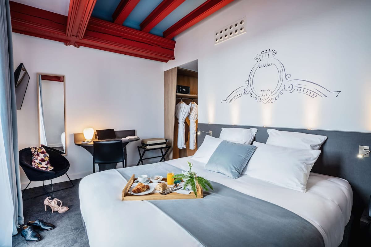 A hotel room with a bed, bedside table, chair, and a desk with a laptop.