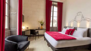 A hotel room with a bed, a desk, a chair, and a window with curtains.