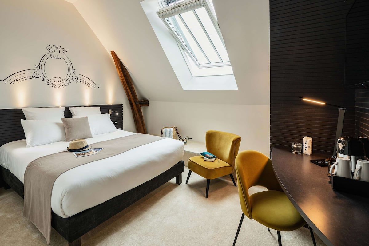 A bedroom with a bed, a desk, a chair, a skylight, and a decorative wall piece.