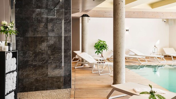 A modern indoor pool area with lounge chairs, a stone wall, and a wooden floor.