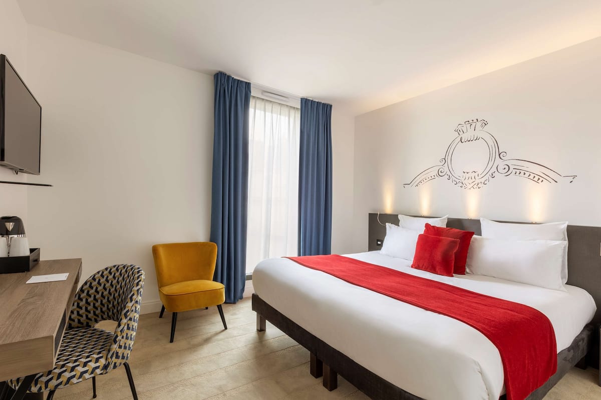 A hotel room with a large bed, a desk with a chair, a television, and a window with curtains.