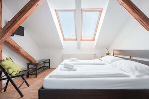 A bedroom with two beds, wooden beams, a skylight, a radiator, and a green chair. - Atik Rooms (Ljubljana)