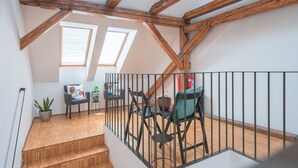 A wooden staircase leading to a loft with a black metal railing, a small table with chairs, and a potted plant. - Atik Rooms (Ljubljana)