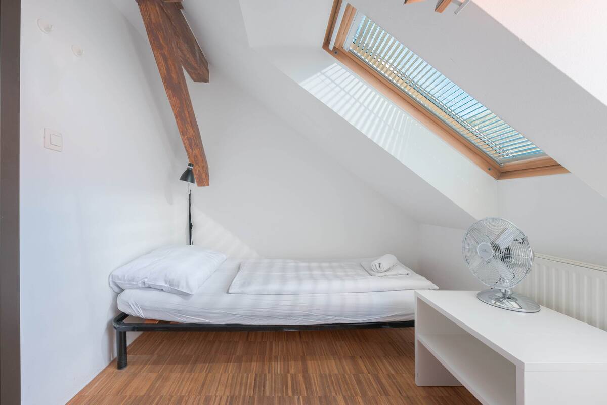A small, neatly arranged room with a bed, a desk, and a radiator.