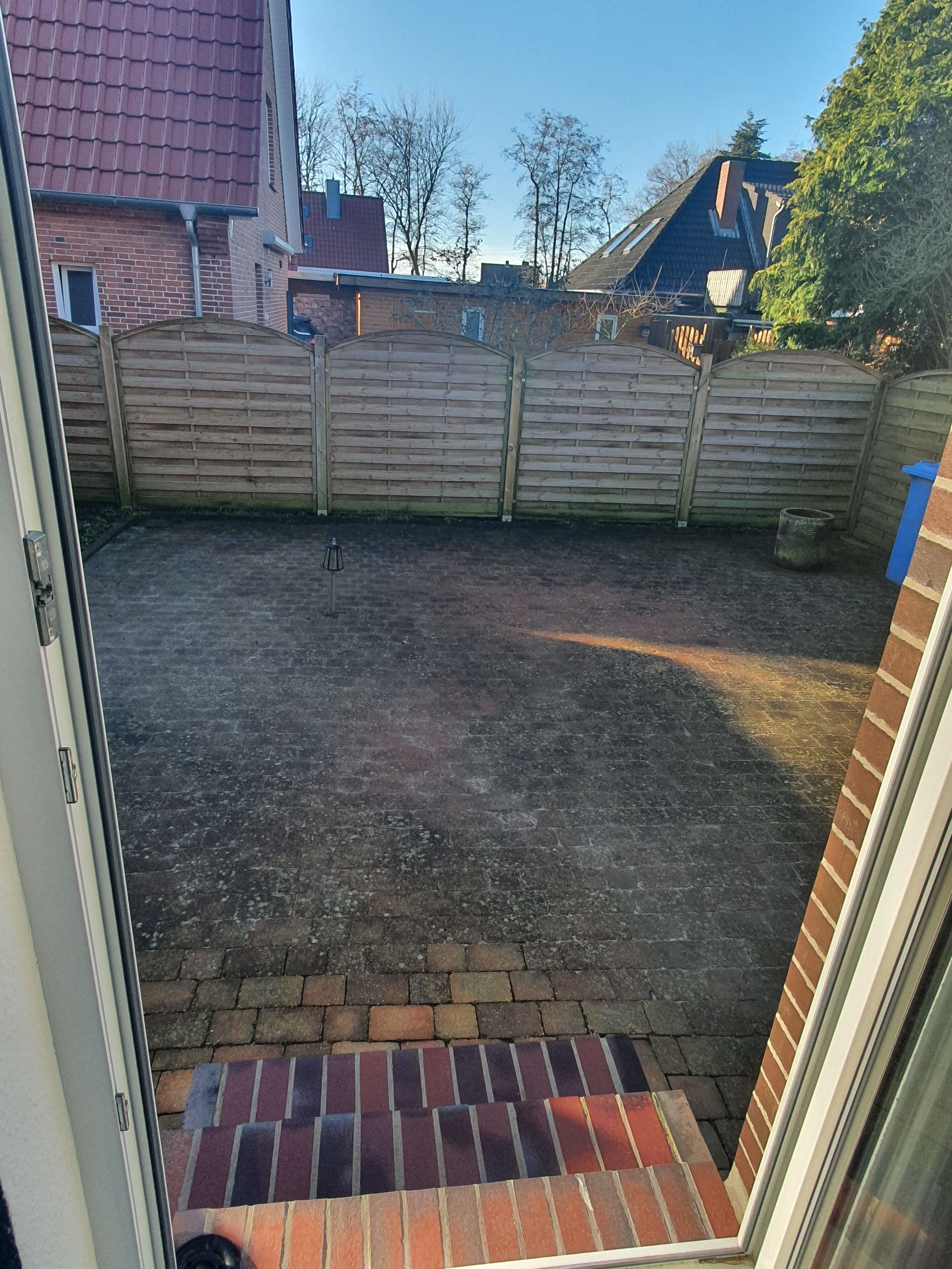 A backyard with a brick patio, a wooden fence, and a view of neighboring houses.