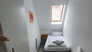 Una habitación pequeña y estrecha con una cama, una ventana y una silla.