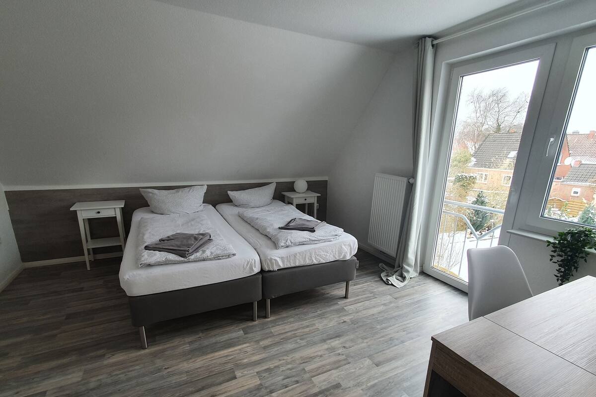 Een moderne slaapkamer met twee bedden, een klein tafeltje en een groot raam met uitzicht op gebouwen.