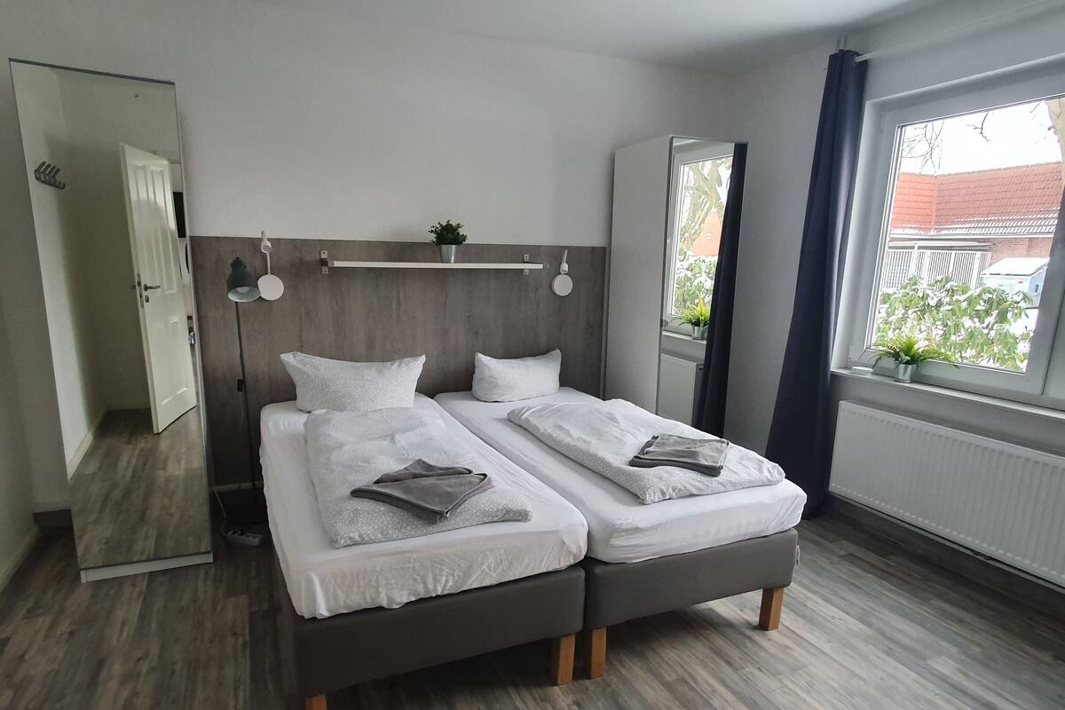 Een moderne slaapkamer met twee bedden, een houten hoofdbord, een nachtkastje met een lamp en een raam met uitzicht.