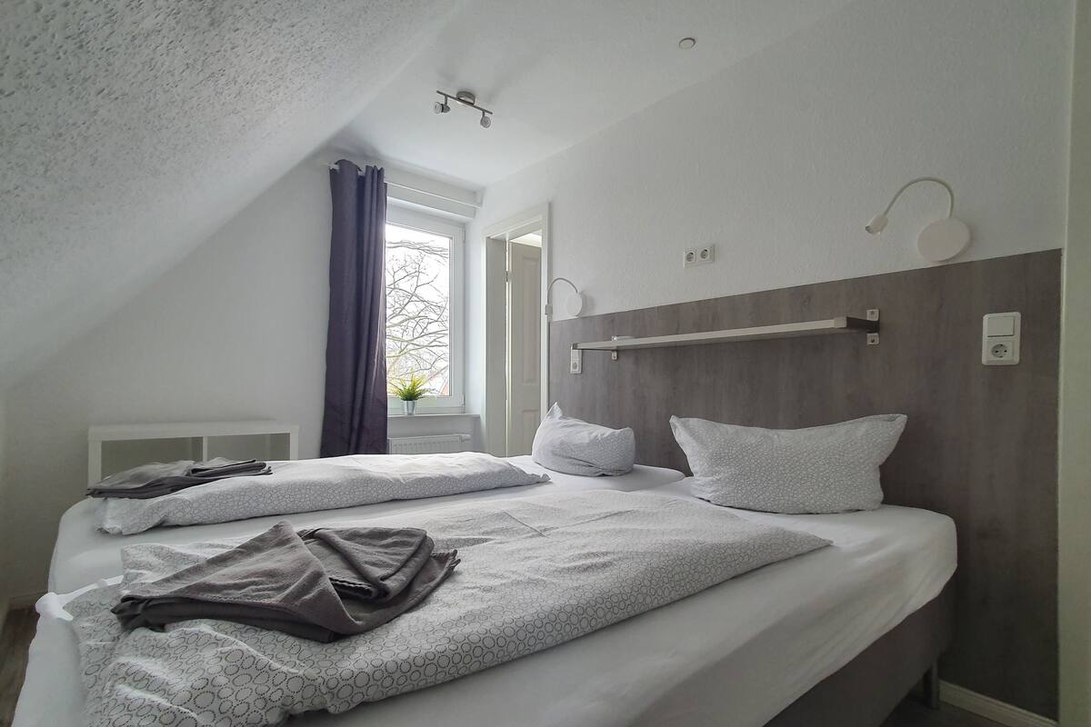 Een moderne slaapkamer met twee bedden, een groot raam en een plafondlamp.