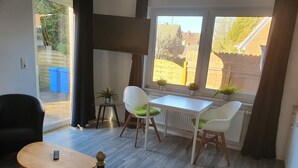 A modern living room with a white table and two white chairs, a small round table with a remote control, and a black chair. - Krabbenkieker (Norden)