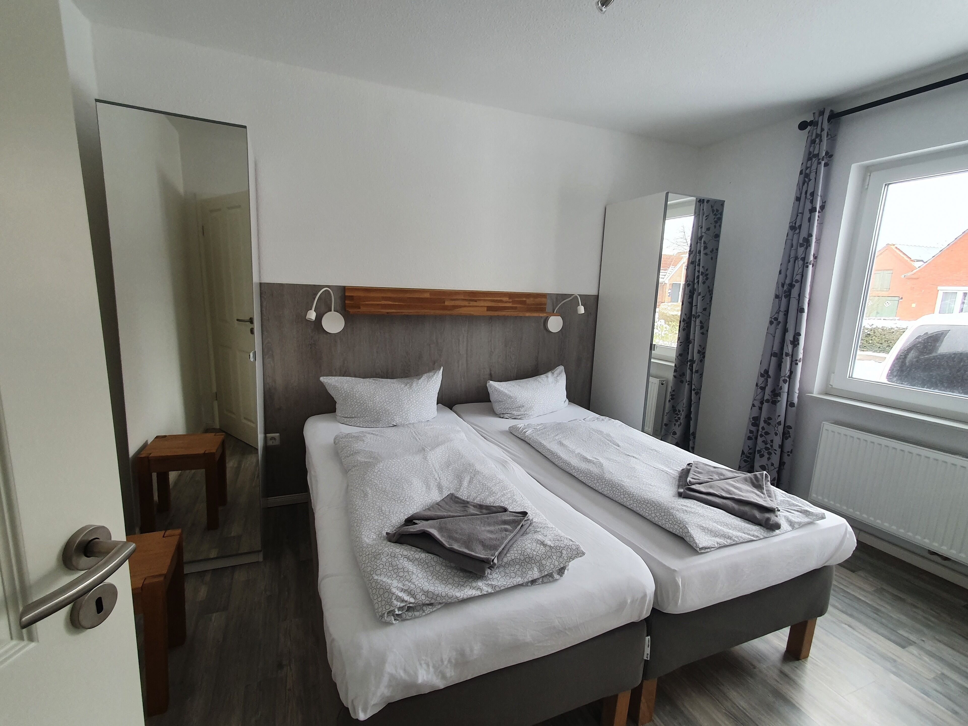 Ein Doppelbett mit Holz-Kopfteil, zwei Nachttische, ein Spiegel und ein Fenster mit Vorhängen.
