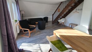 A modern living room with a sofa, chairs, a dining table, and a staircase. - Krabbenkieker (Norden)