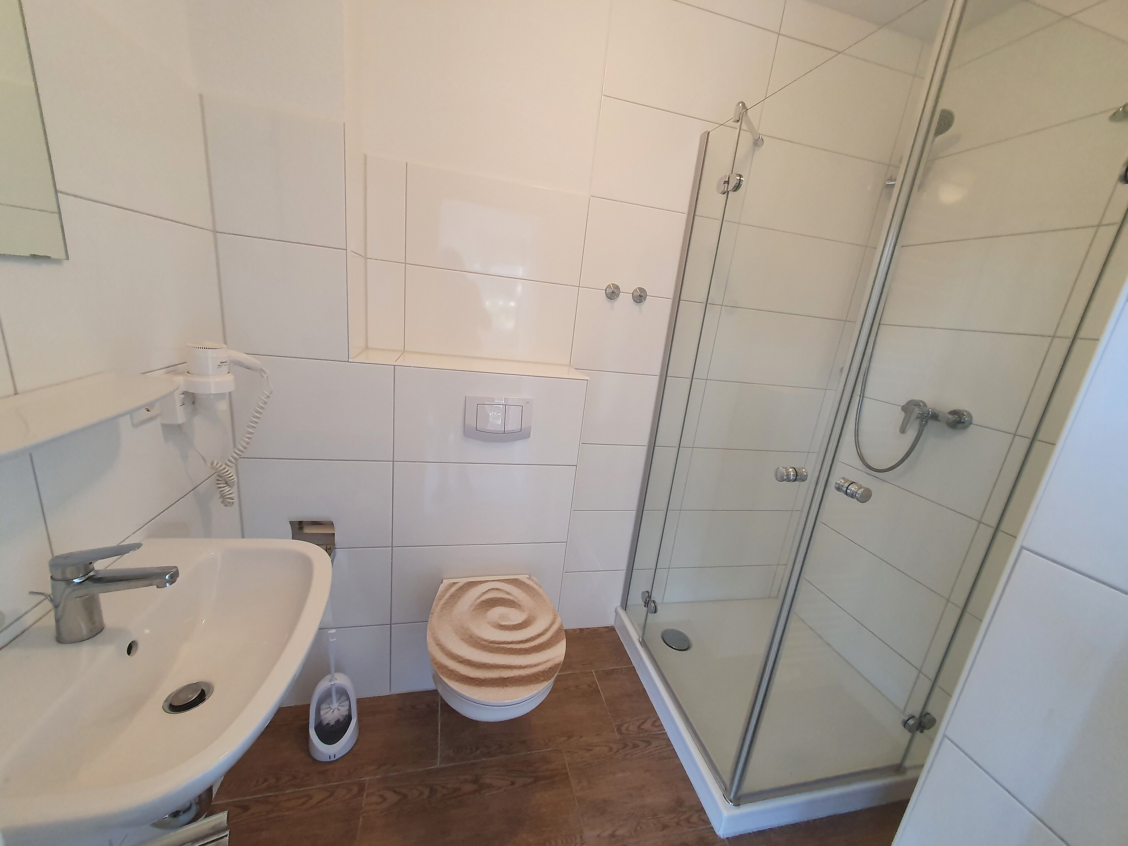 Une salle de bain avec un lavabo blanc, des toilettes et une douche fermée par une paroi de verre.