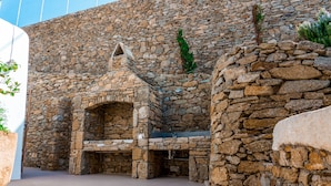 Un bâtiment en pierre doté d’une cheminée, d’un banc et d’un petit espace aménagé en jardin.