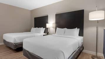 A hotel room with two beds, a nightstand with a lamp, and a floor lamp.
