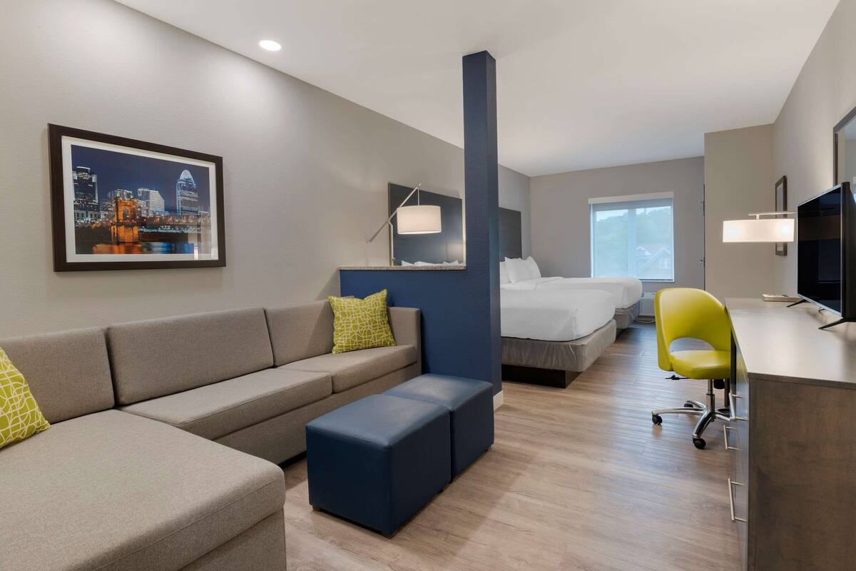 A modern hotel room with a sofa, a bed, a desk, and a cityscape painting.