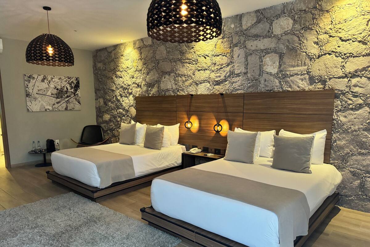 Une chambre d’hôtel moderne avec deux lits, un mur en pierre et un grand tableau.