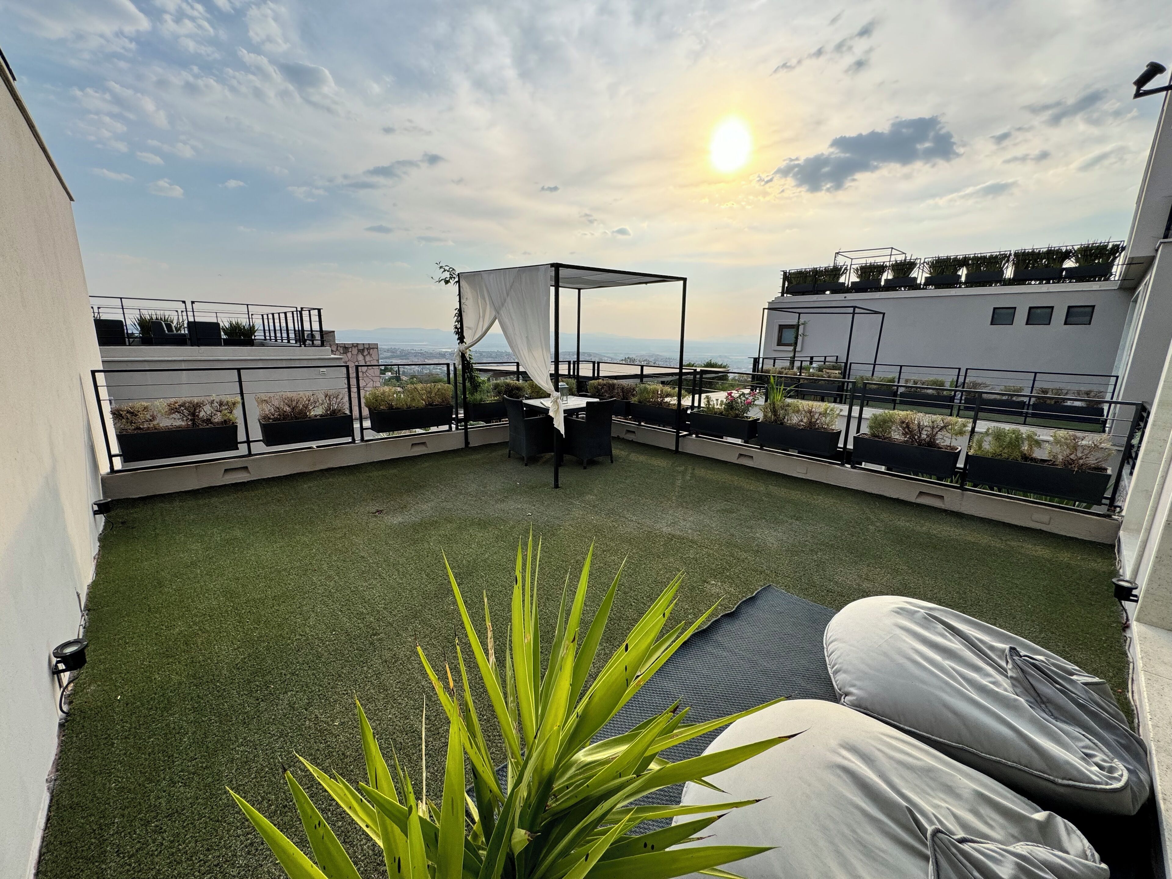 A rooftop terrace with artificial grass, a covered seating area, and potted plants.