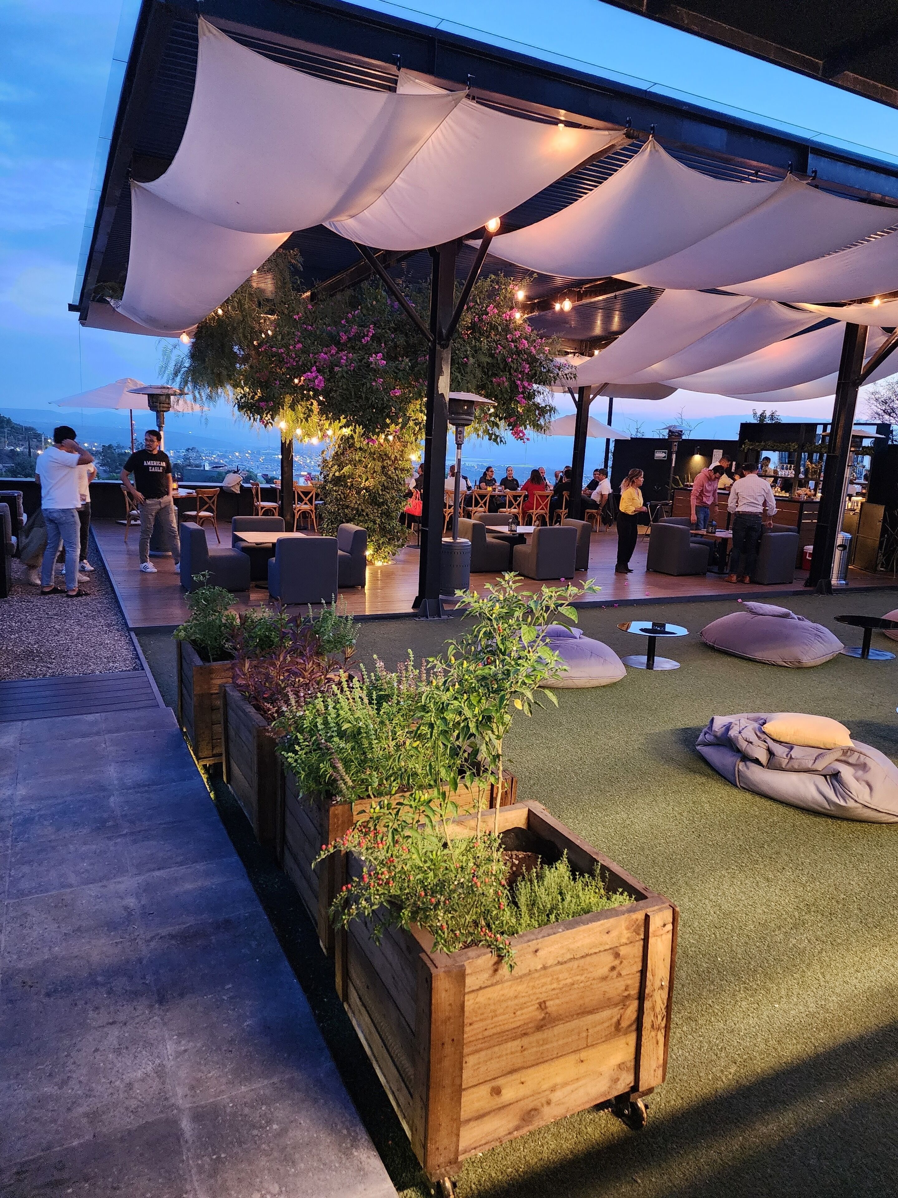An outdoor seating area with wooden planters, tables, and chairs under a covered patio.