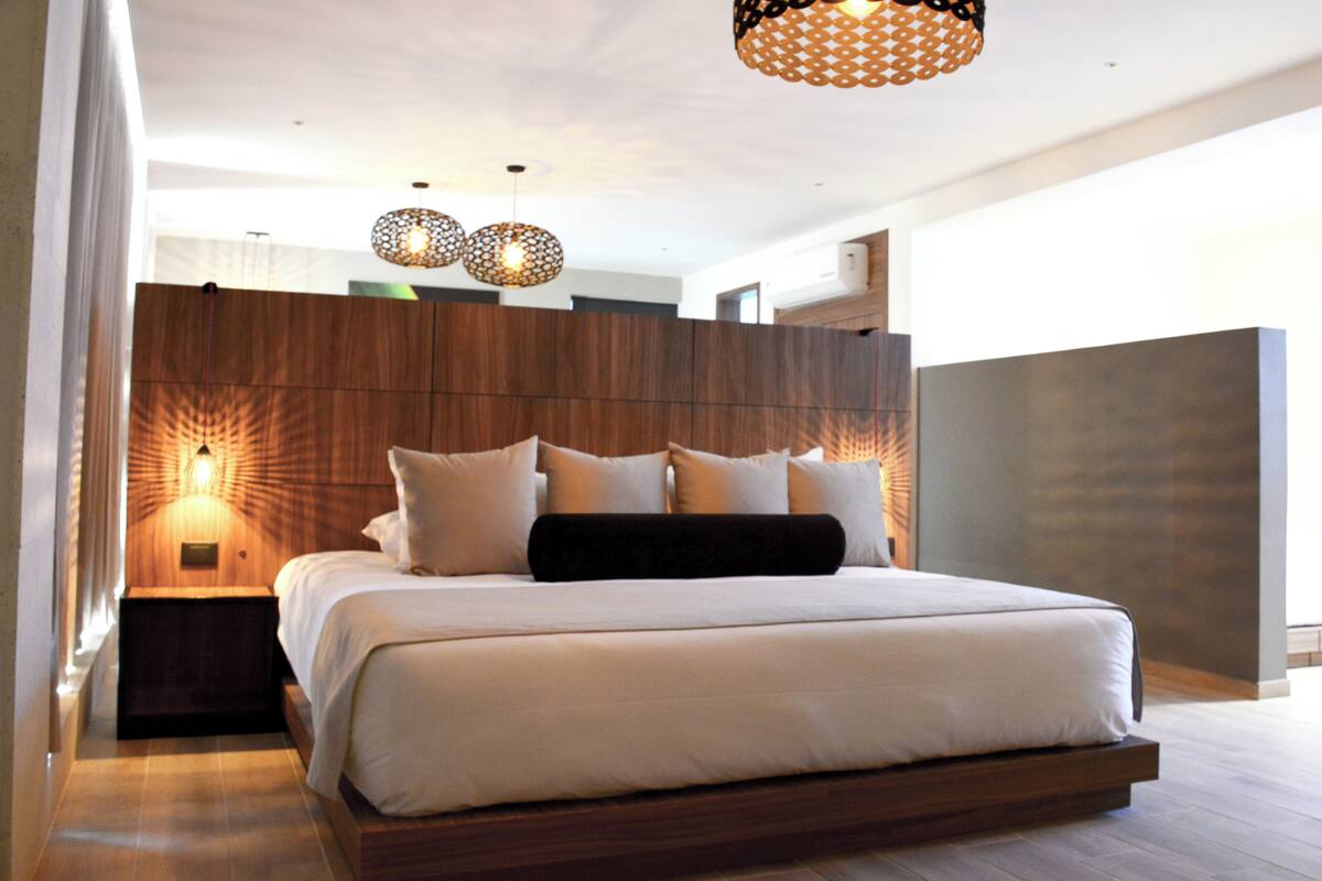 Une chambre moderne avec un grand lit, une tête de lit en bois et un luminaire suspendu.