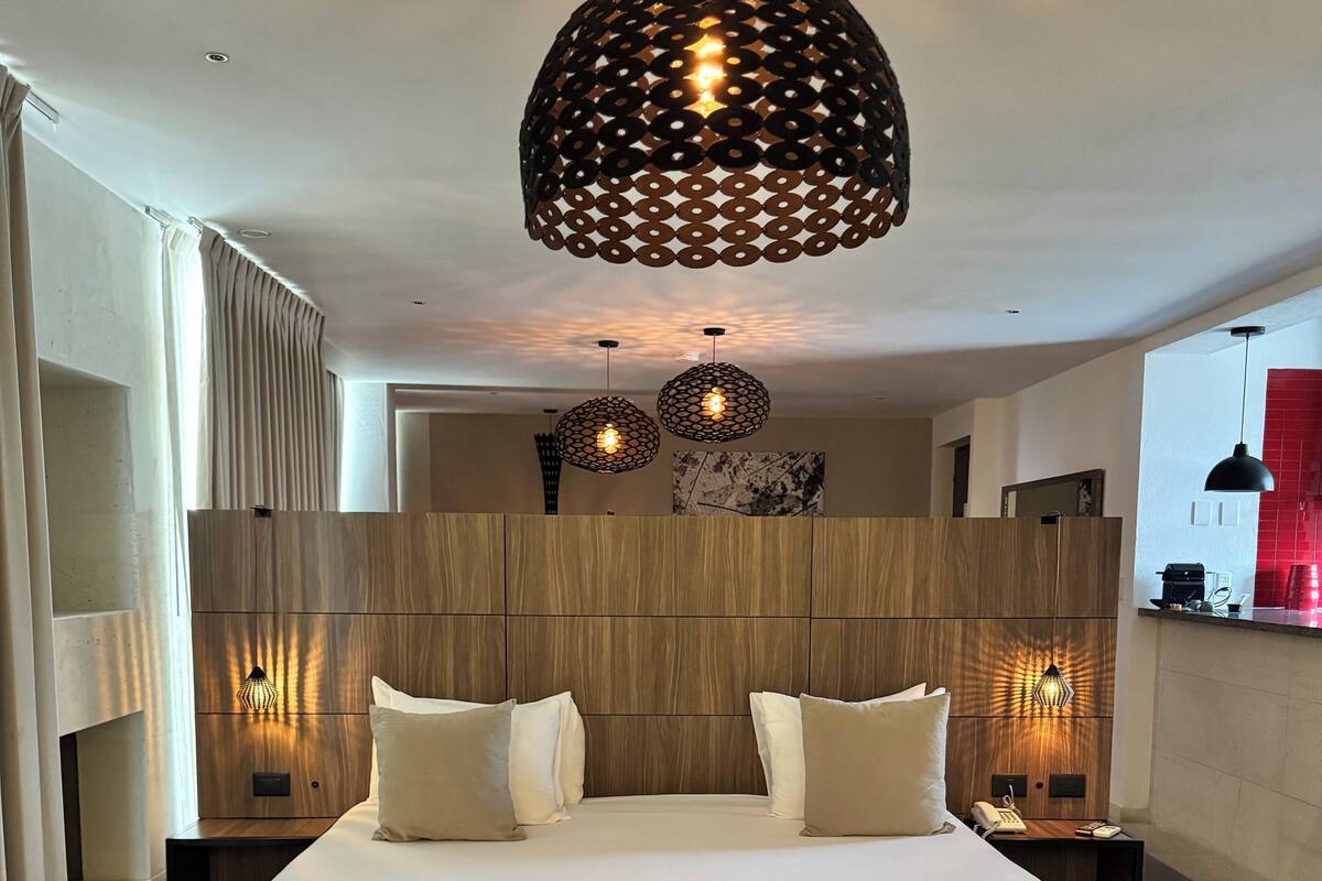 Une chambre d’hôtel moderne avec un grand lit, une tête de lit en bois et des luminaires suspendus.