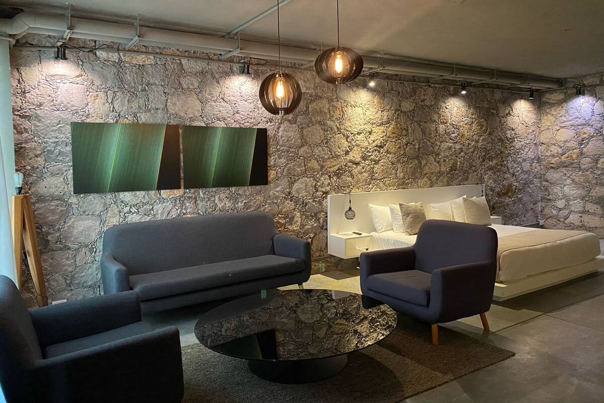 Un salon moderne avec un mur en pierre, un canapé gris, une table basse ronde et deux fauteuils.