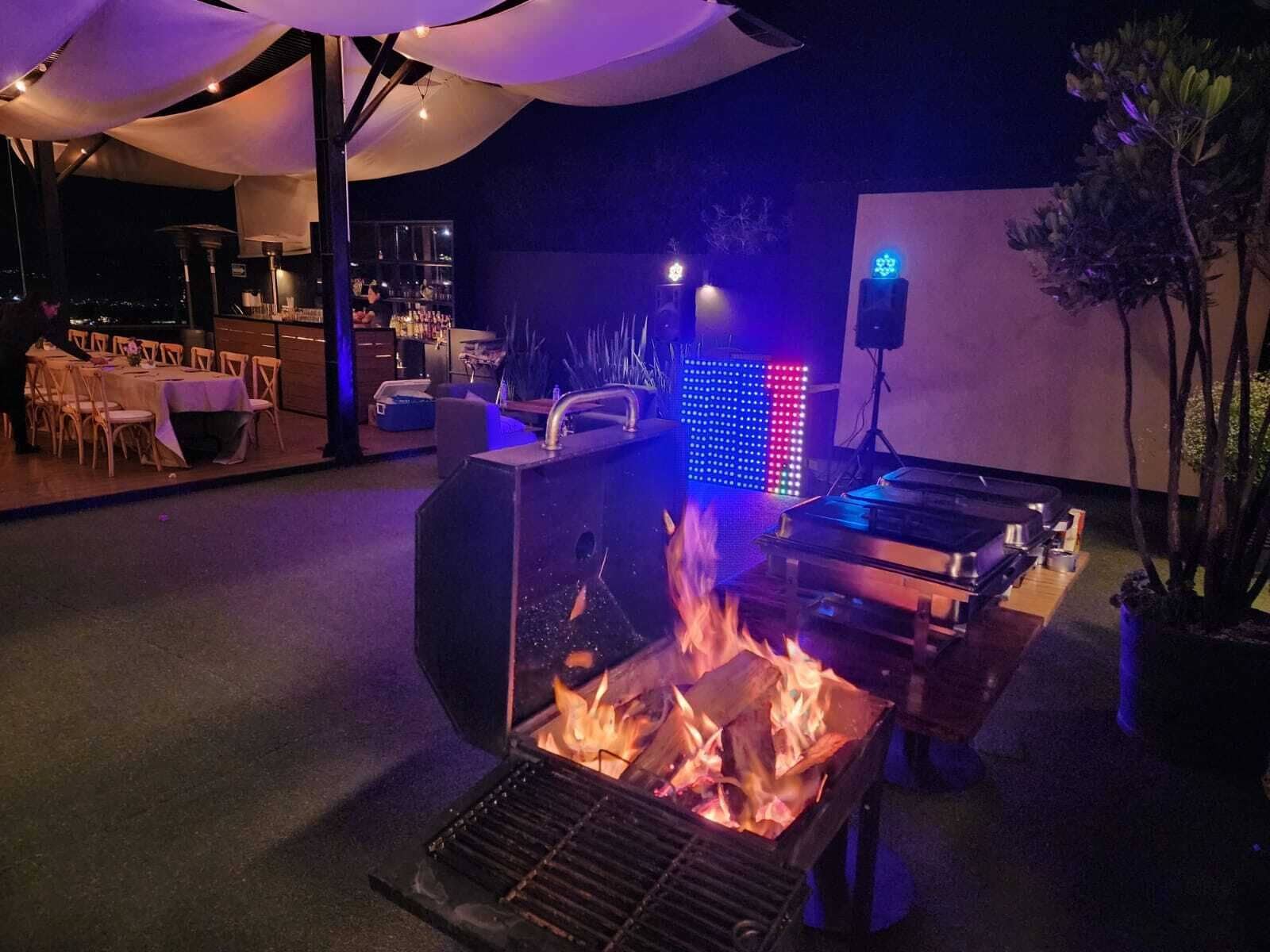 An outdoor dining area with a fire feature, tables, chairs, and a bar area in the background.