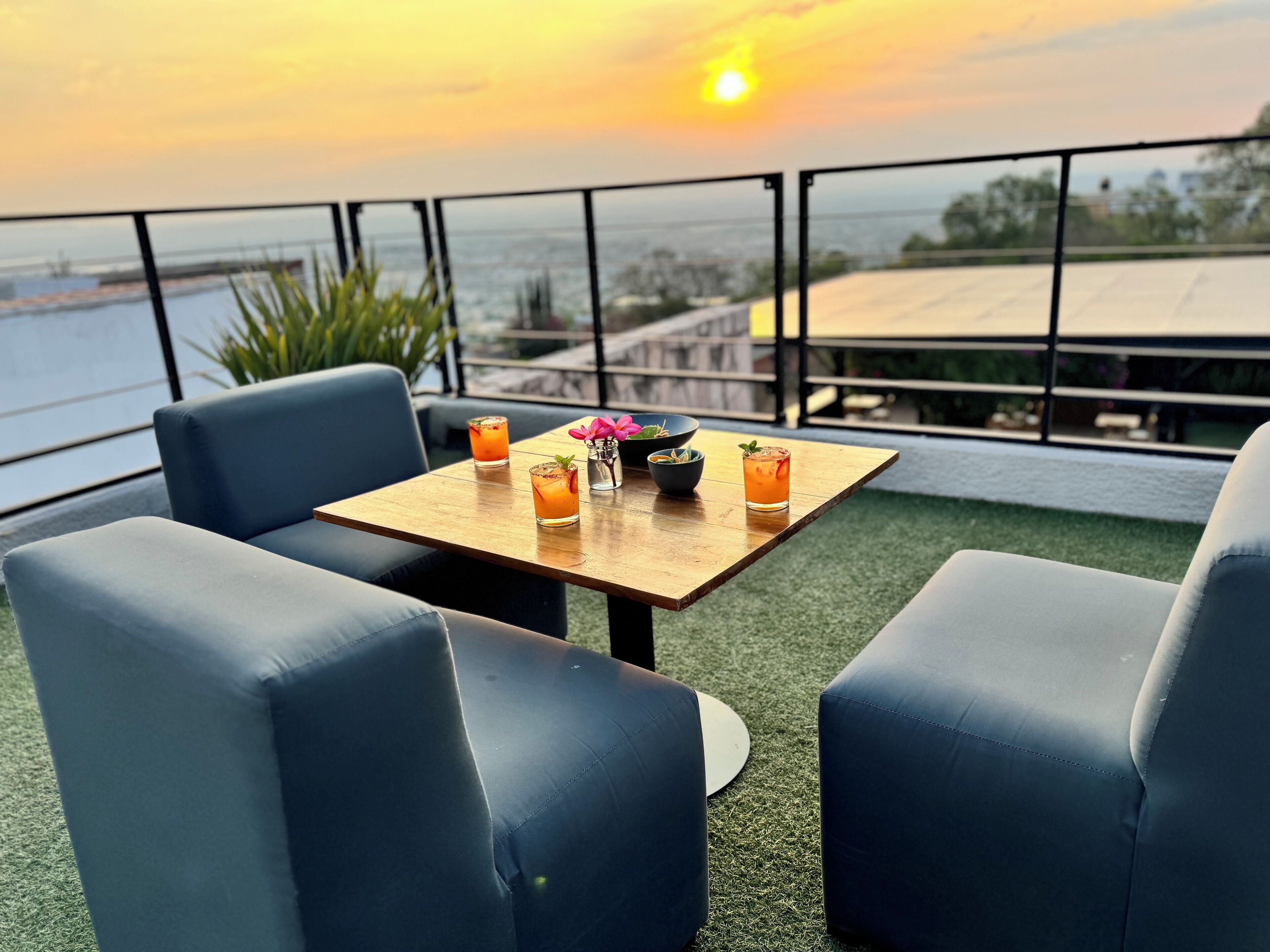 Una terraza con una mesa lista para dos personas, dos bebidas, un florero y vistas al atardecer sobre el agua.