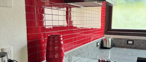 A kitchen with red tiled backsplash, stainless steel range hood, granite countertop, and a window with a view.