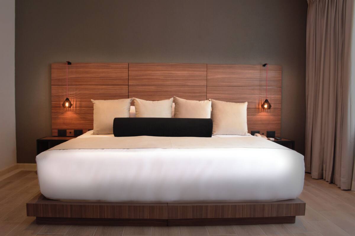 Une chambre d’hôtel moderne avec un grand lit, une tête de lit en bois et deux tables de chevet avec des lampes.