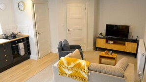 Een woonkamer met een bank, een televisie, een salontafel en een keuken met een fornuis.