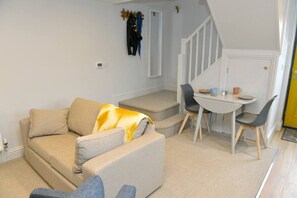 A living room with a sofa, a coffee table, and a staircase leading to a dining area. - Nest House, Free Parking Super cosy one bedroom (Cambridgeshire)