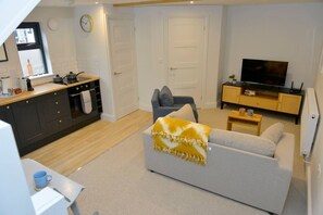 A modern living room with a sofa, a television, a kitchen area, and a dining table. - Nest House, Free Parking Super cosy one bedroom (Cambridgeshire)