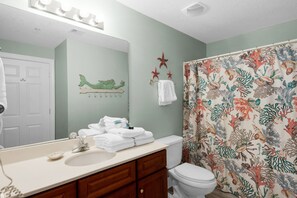 Features a large mirror above the sink, a white toilet, and a shower curtain with a sea life pattern.