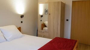 Une chambre à coucher avec un lit, une couverture rouge, une armoire, un miroir et une porte en bois.