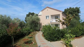 Un bâtiment à deux étages doté d’un balcon, entouré d’un jardin avec un chemin sinueux.