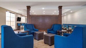 A modern hotel lobby with blue armchairs, round tables, and a patterned carpet.