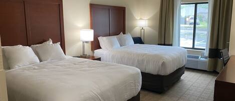 A hotel room with two beds, a large window with curtains, a flat-screen TV, and a desk with a lamp.