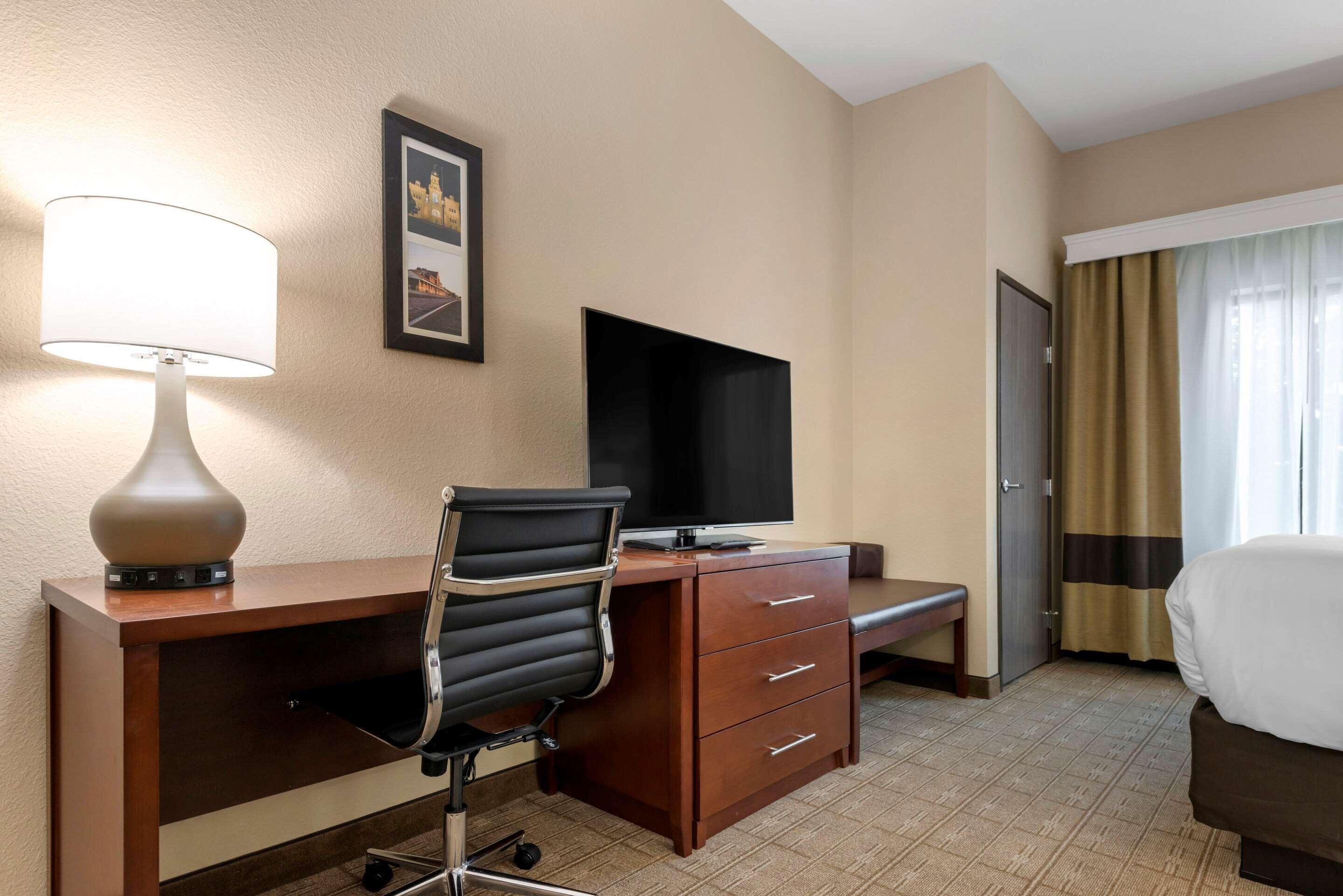 A hotel room with a desk, a chair, a television, a bed, and a window with curtains.