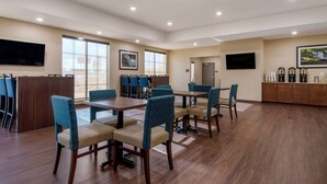 A spacious conference room with wooden tables and blue upholstered chairs, large windows, and a flat-screen TV mounted on the wall.