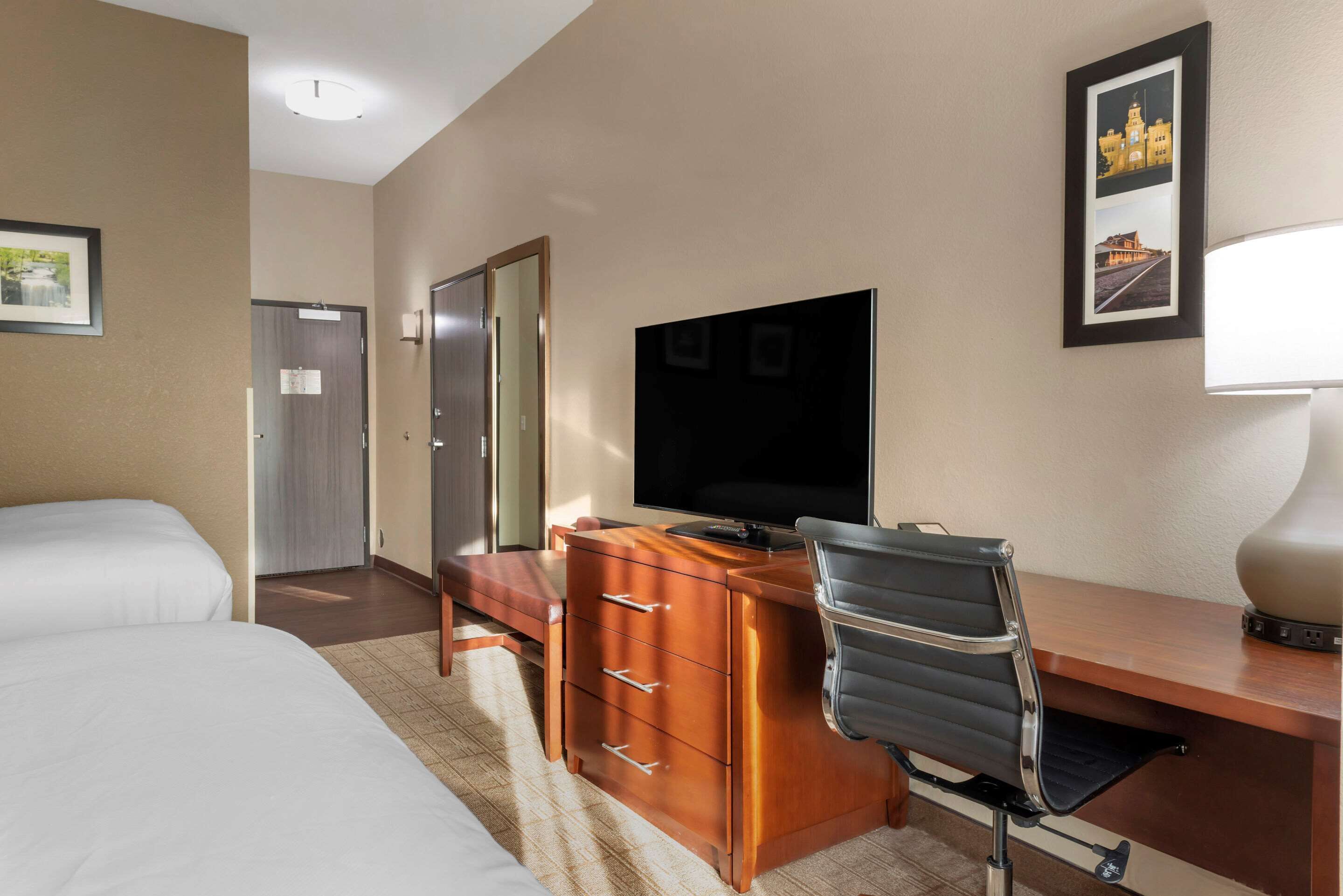 A hotel room with a bed, a desk with a chair, a television, a dresser, and a mirror.