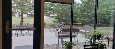 A room with large windows offering a view of an outdoor patio with tables and chairs, and a door leading outside.