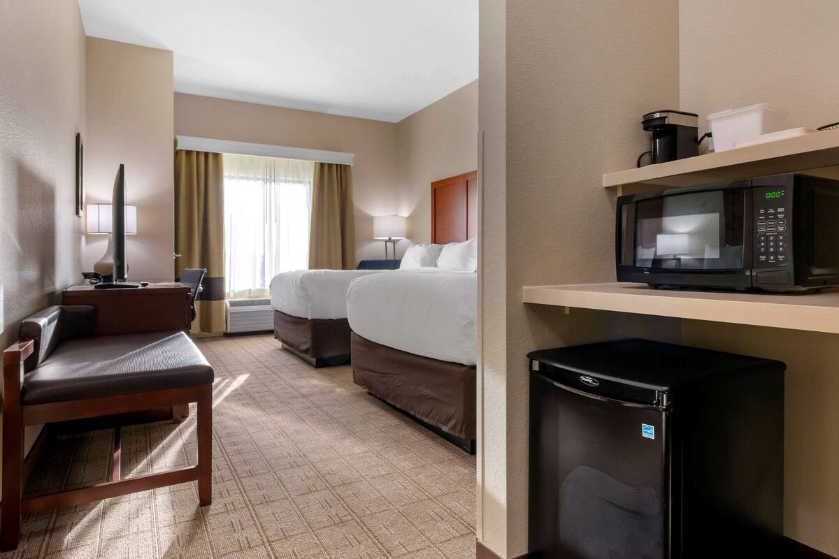 Ein Hotelzimmer mit einer Couch, zwei Betten, einer Mikrowelle, einem Kühlschrank, einem Fernseher und einem Fenster mit Vorhängen.