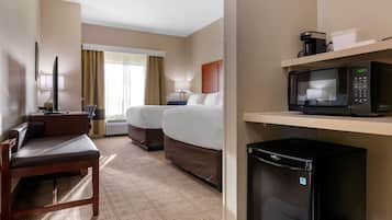 A hotel room with a sofa, two beds, a microwave, a refrigerator, a television, and a window with curtains.