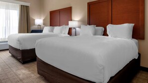A hotel room with two large beds, a window with curtains, and a wall-mounted lamp.