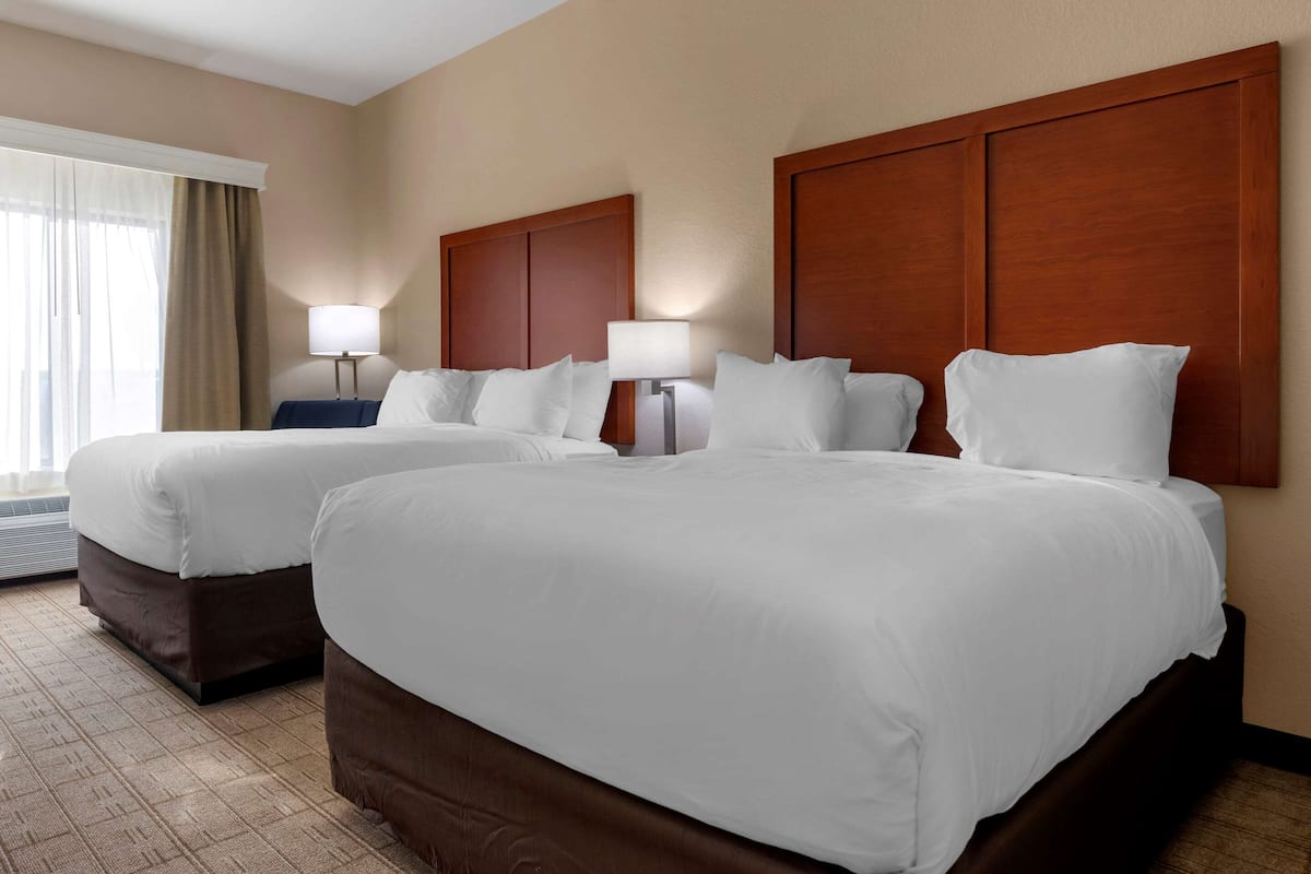 Ein Hotelzimmer mit zwei großen Betten, einem Vorhangfenster und einer Wandlampe.