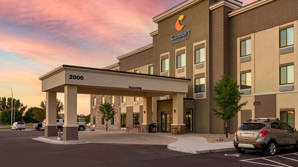 A Comfort Inn & Suites building with a covered entrance, numbered 2000, and a parking lot with cars.