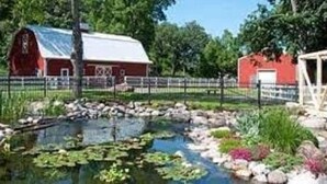 A barn with a metal roof and a fenced area with a pond and rocks.