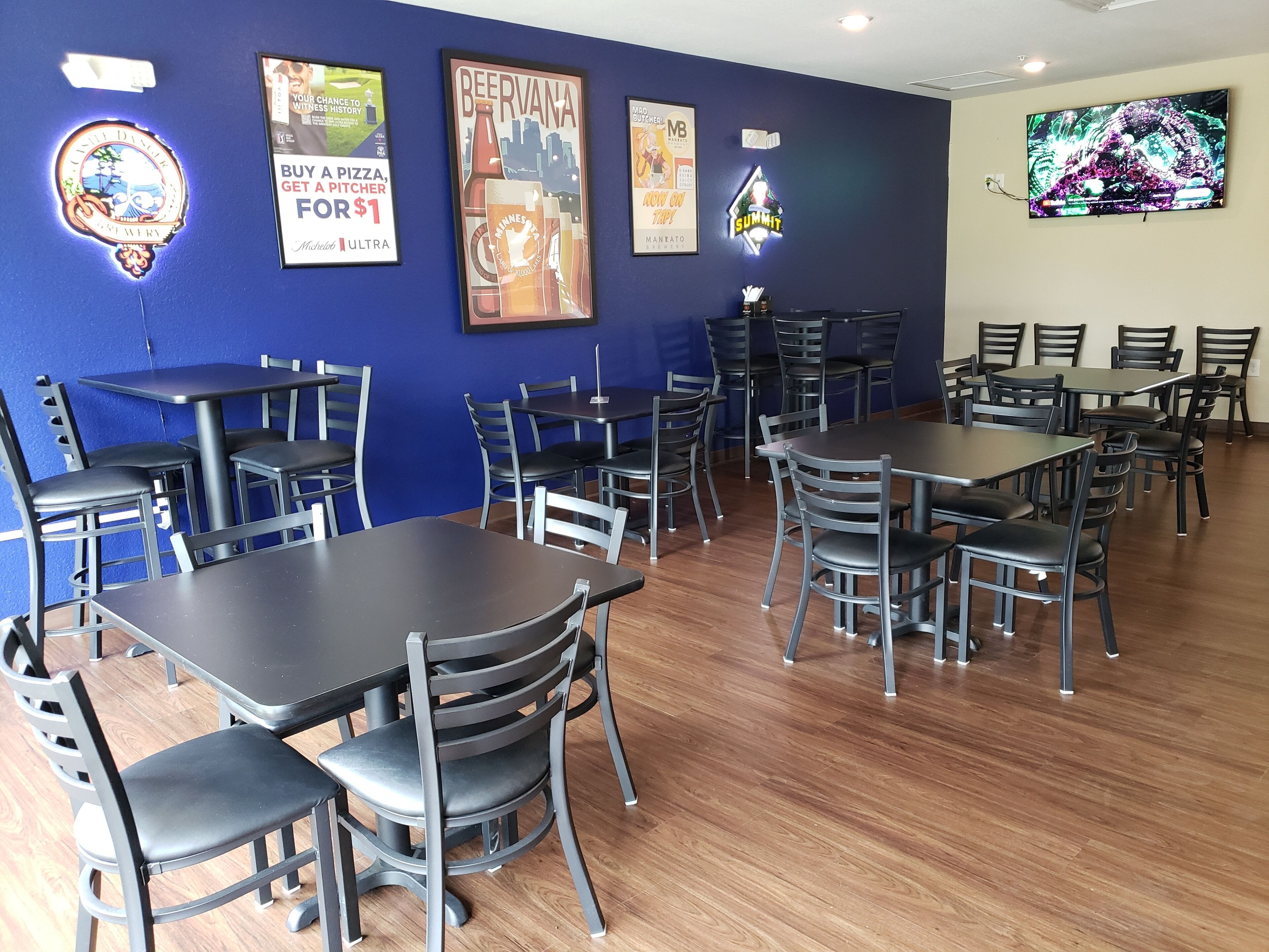 Un restaurante con varias mesas y sillas, carteles enmarcados en la pared y una pantalla de televisión.