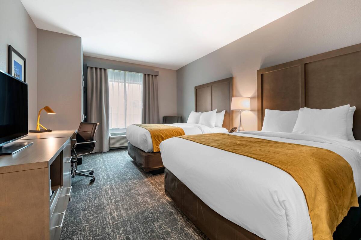 Una habitación de hotel con dos camas, un escritorio con televisor, una silla y una ventana con cortinas.